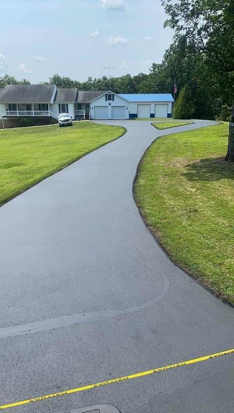 Two-story suburban house with blue metal roof, white exterior, and detached garage set on manicured lawn with curved driveway