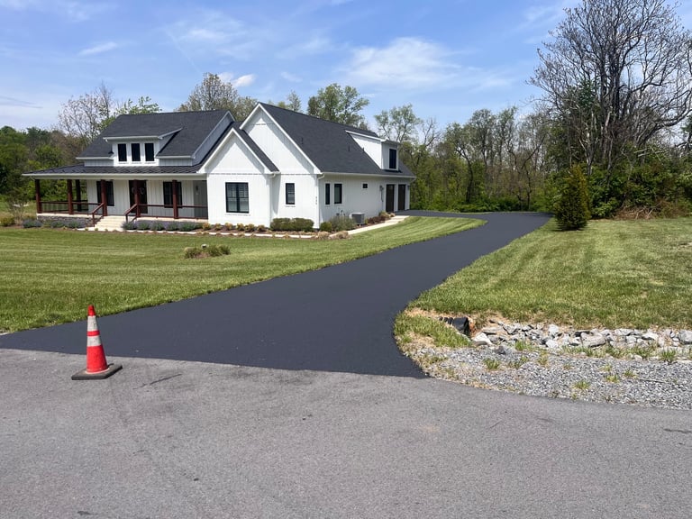 New asphalt driveway being paved in front of a white farmhouse