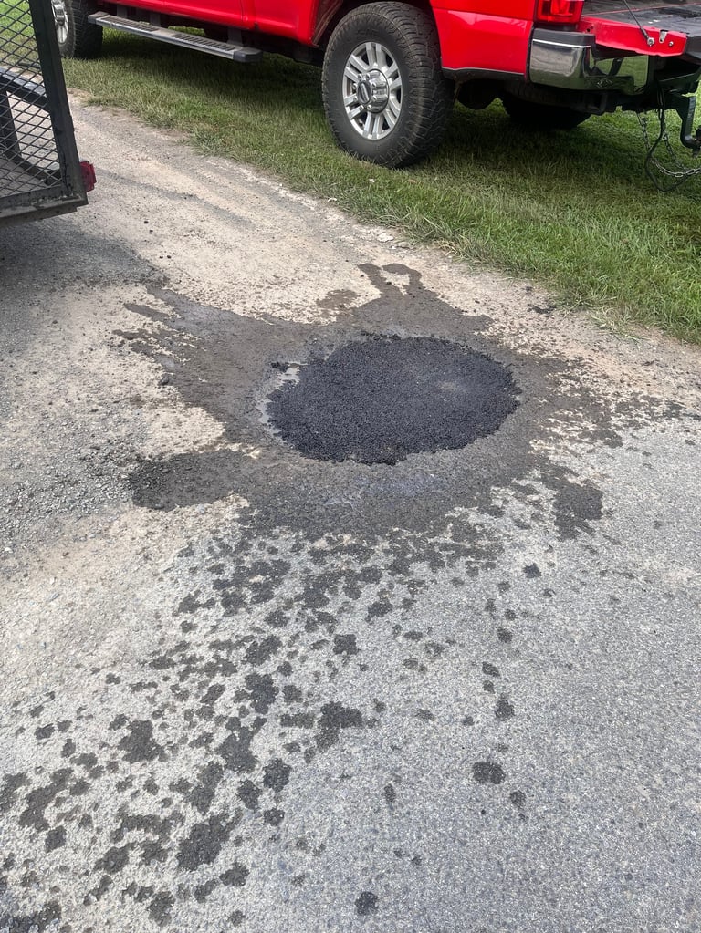 Large pothole in asphalt driveway with red pickup truck parked nearby